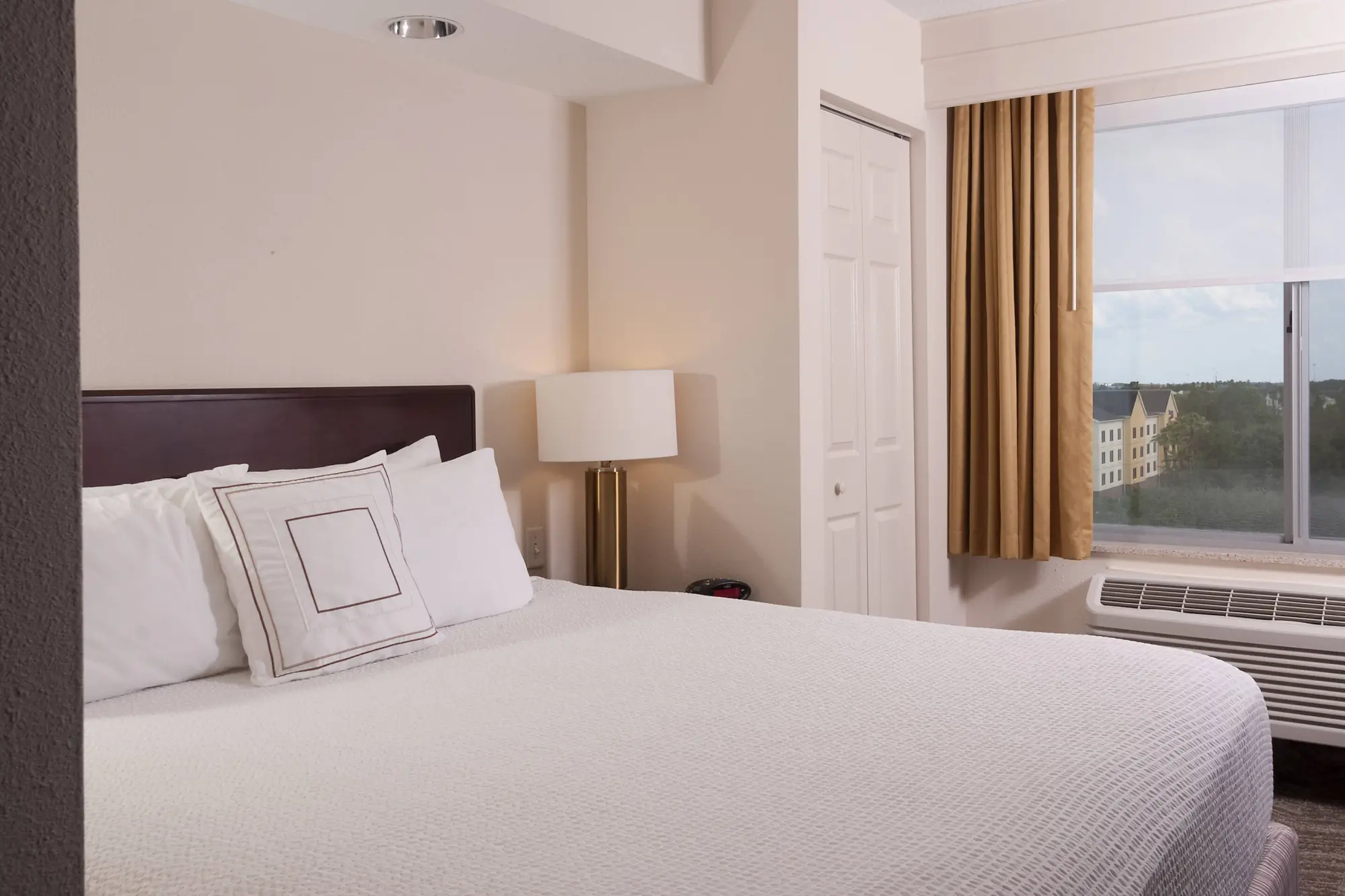 Bright and cozy king room at SpringHill Suites by Marriott featuring a bed with white linens, accent pillow, bedside lamp, and a window with beige curtains overlooking the outside.