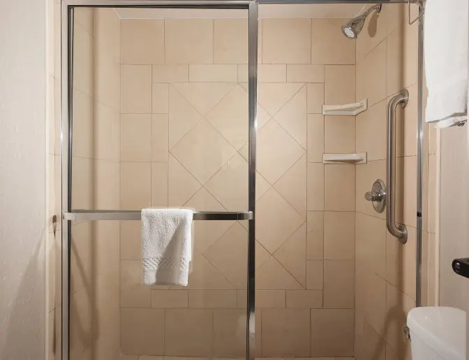 SpringHill Suites by Marriott bathroom showcasing a large, tiled walk in shower with glass doors, built-in shelves, a towel bar, and a safety grab bar.