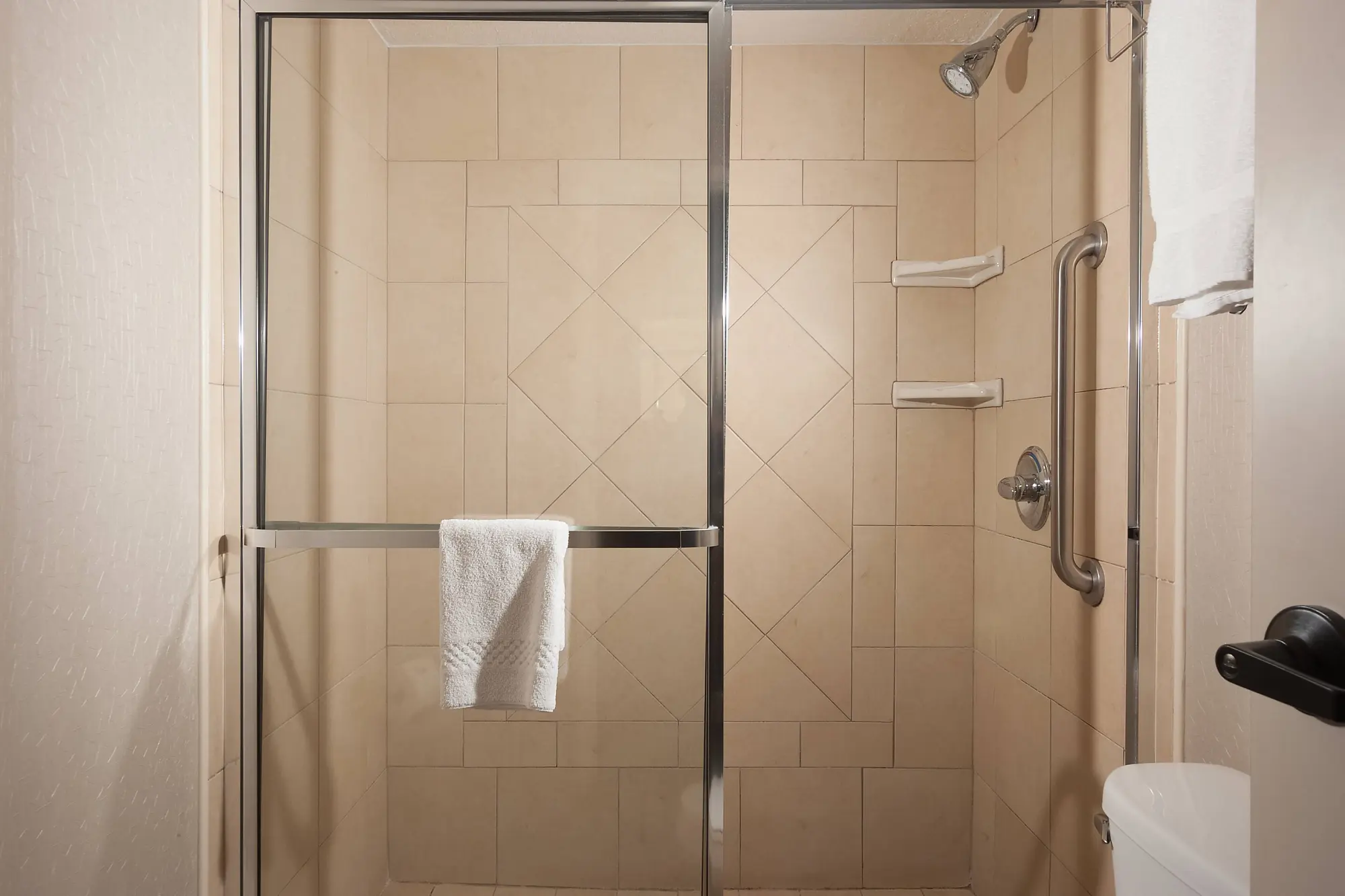 SpringHill Suites by Marriott bathroom showcasing a large, tiled walk in shower with glass doors, built-in shelves, a towel bar, and a safety grab bar.