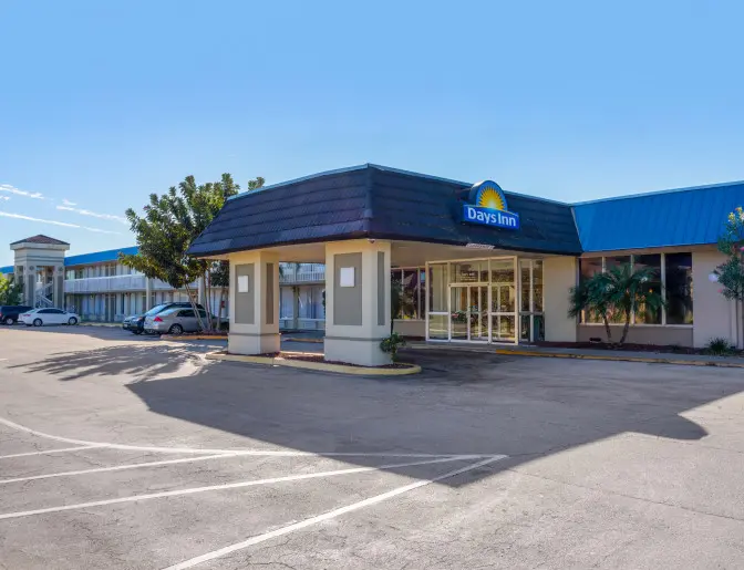 Front view of the Days Inn Titusville hotel under a clear sky, showing the entrance with a covered drive-up area and a parking lot with multiple vehicles.