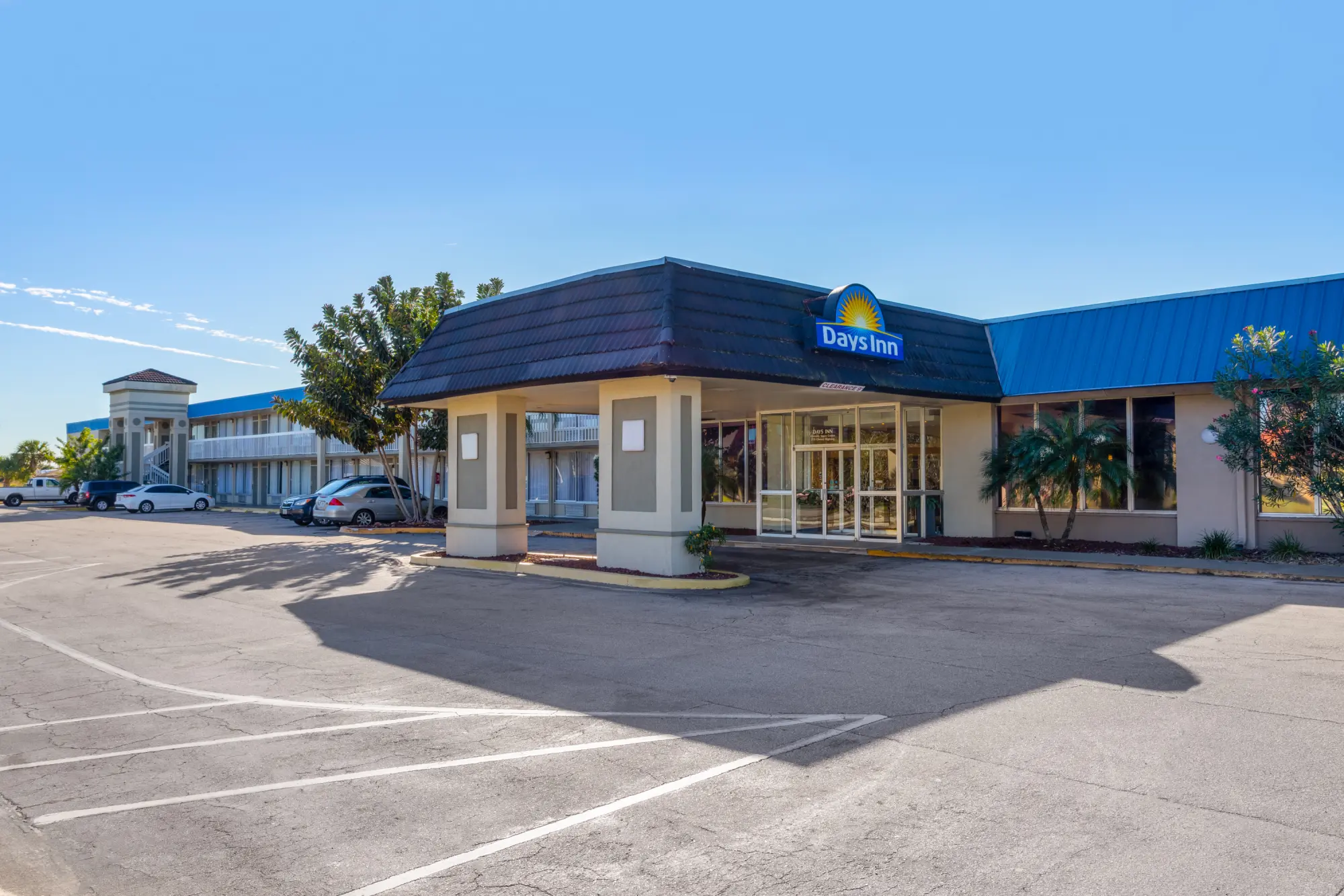 Front view of the Days Inn Titusville hotel under a clear sky, showing the entrance with a covered drive-up area and a parking lot with multiple vehicles.