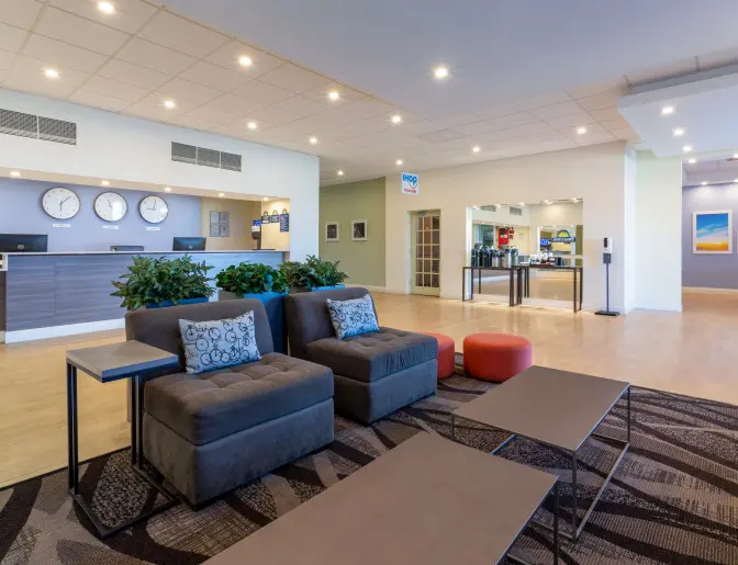 Lobby of the Days Inn Titusville hotel featuring a modern reception desk with clocks showing different time zones, a comfortable seating area with plush chairs and tables