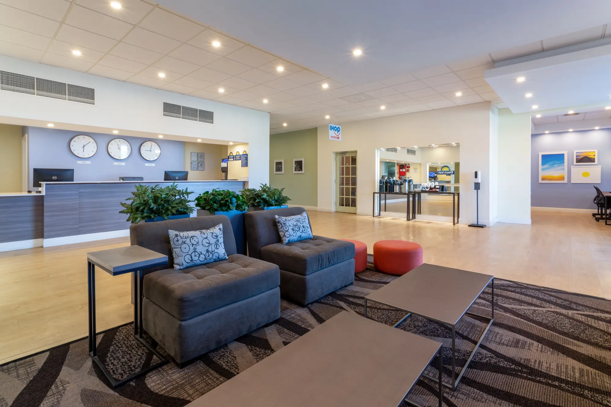 Lobby of the Days Inn Titusville hotel featuring a modern reception desk with clocks showing different time zones, a comfortable seating area with plush chairs and tables