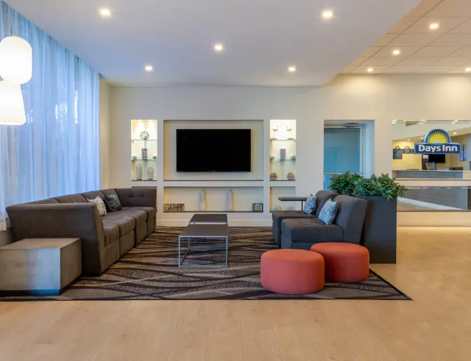Lobby of the Days Inn Titusville hotel featuring a comfortable seating area with a large sectional sofa, armchairs, coffee tables, and a wall-mounted TV, with the reception desk visible in the background.