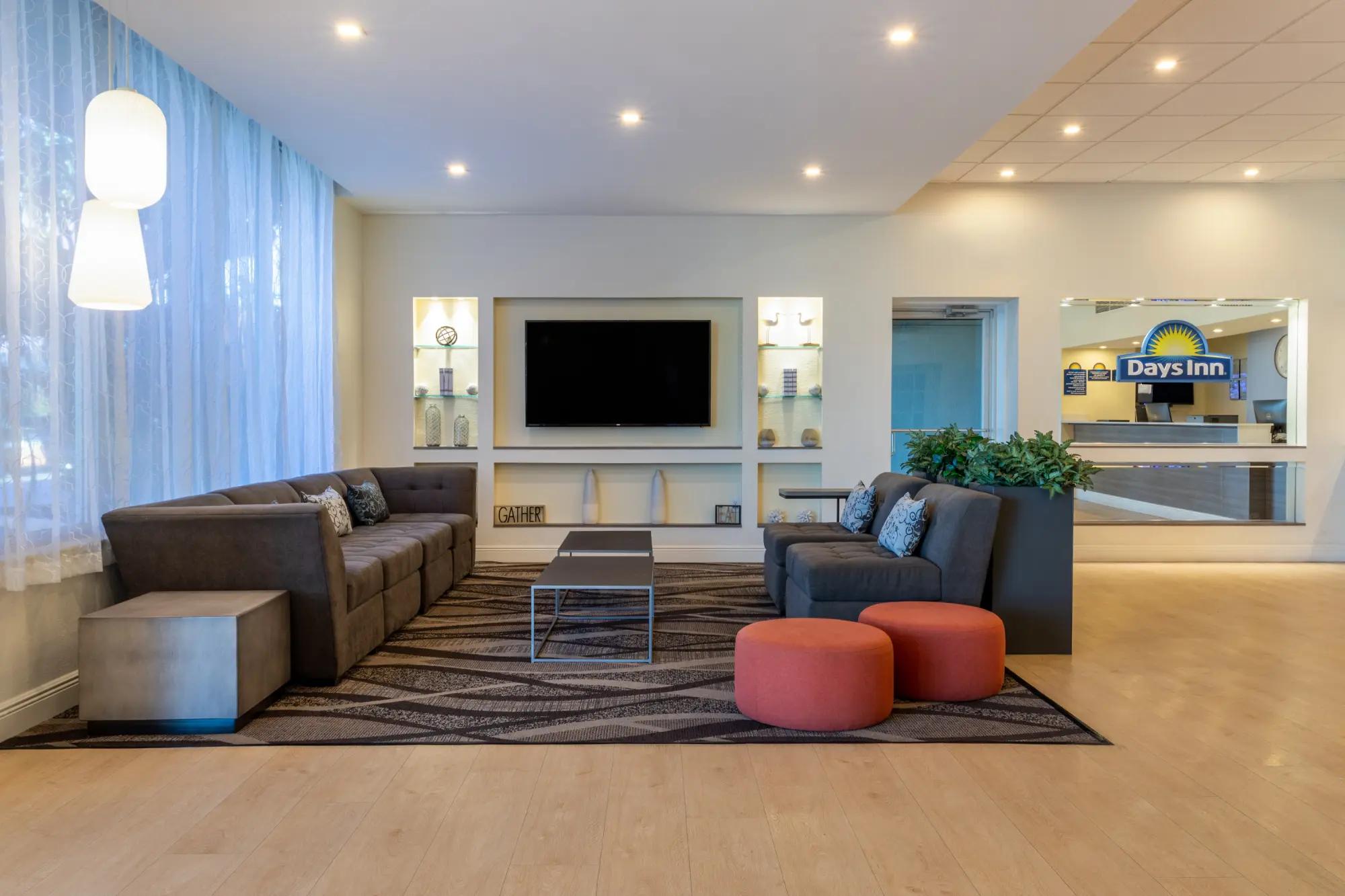 Lobby of the Days Inn Titusville hotel featuring a comfortable seating area with a large sectional sofa, armchairs, coffee tables, and a wall-mounted TV, with the reception desk visible in the background.