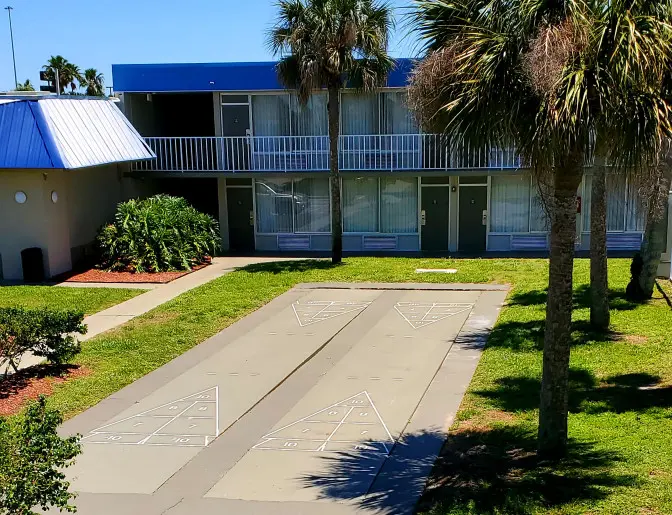 Days Inn Titusville hotel outdoor activity area featuring a shuffleboard court, palm trees, and well-maintained landscaping, with the hotel rooms visible in the background.
