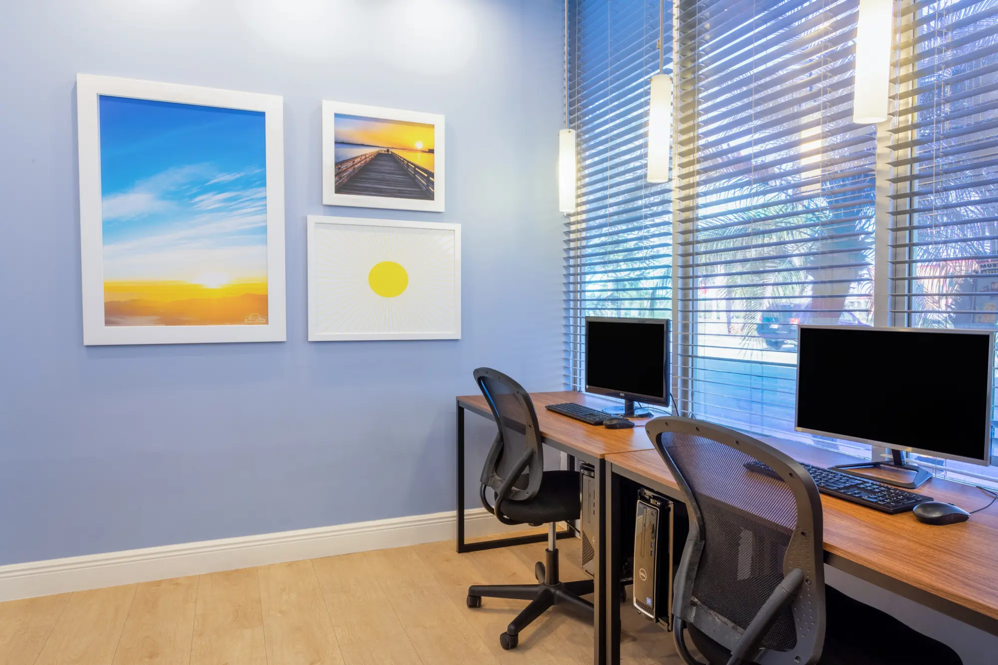 Business center at the Days Inn Titusville hotel featuring two computer workstations with ergonomic chairs, located by a large window with blinds and decorated with framed artwork.