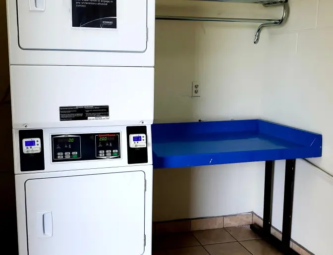 Days Inn Titusville hotel laundry facility with a stackable washer and dryer and a blue folding table, set against a tiled floor and beige walls.