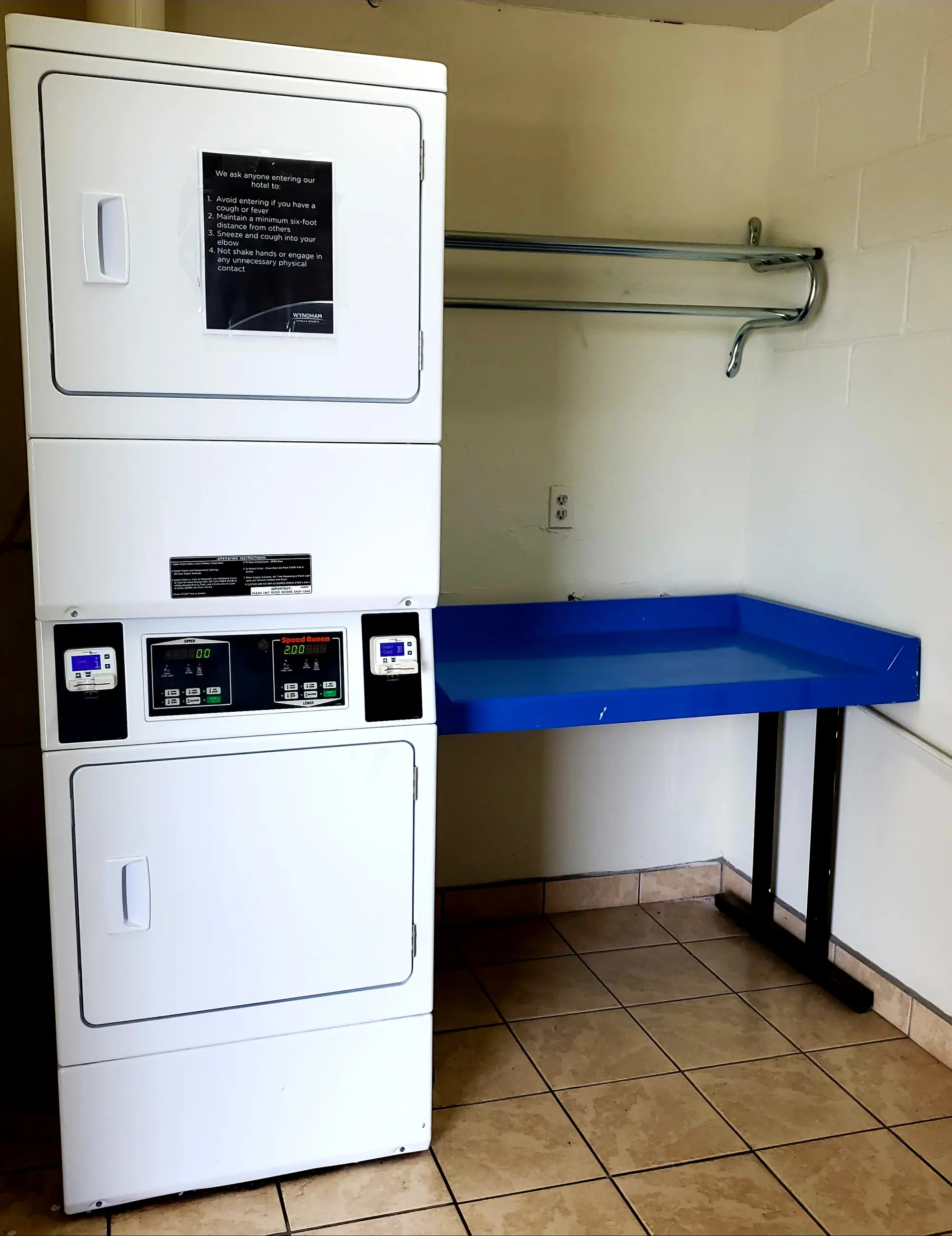 Days Inn Titusville hotel laundry facility with a stackable washer and dryer and a blue folding table, set against a tiled floor and beige walls.