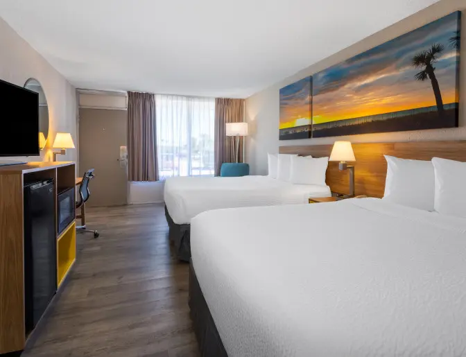 Spacious hotel room at Days Inn Titusville with two queen beds, modern furnishings, a flat-screen TV, and a large window providing natural light.