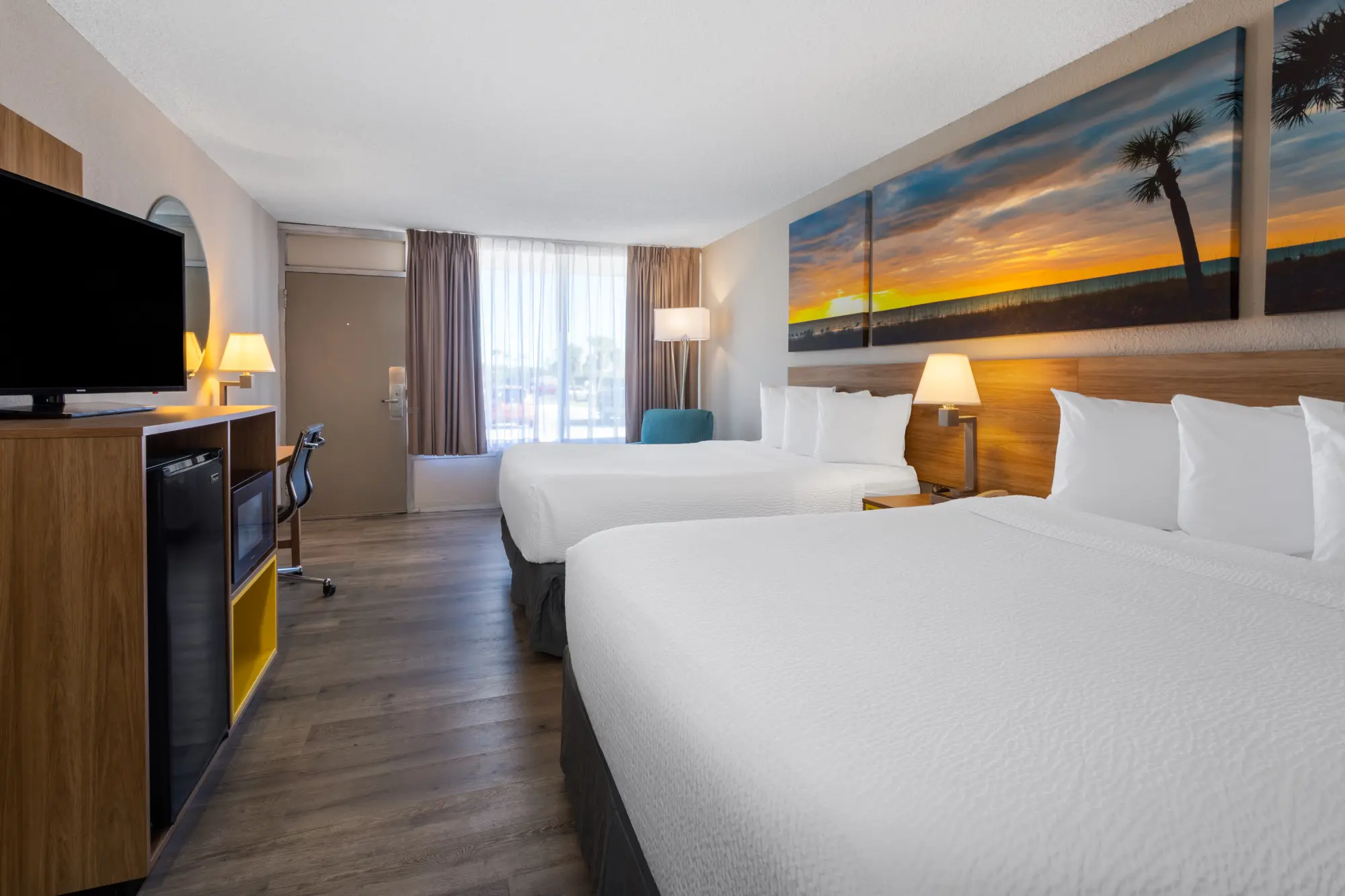 Spacious hotel room at Days Inn Titusville with two queen beds, modern furnishings, a flat-screen TV, and a large window providing natural light.