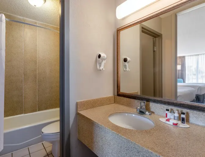 Days Inn Titusville hotel bathroom featuring a granite countertop with a sink, a wall-mounted hairdryer, and complimentary toiletries.