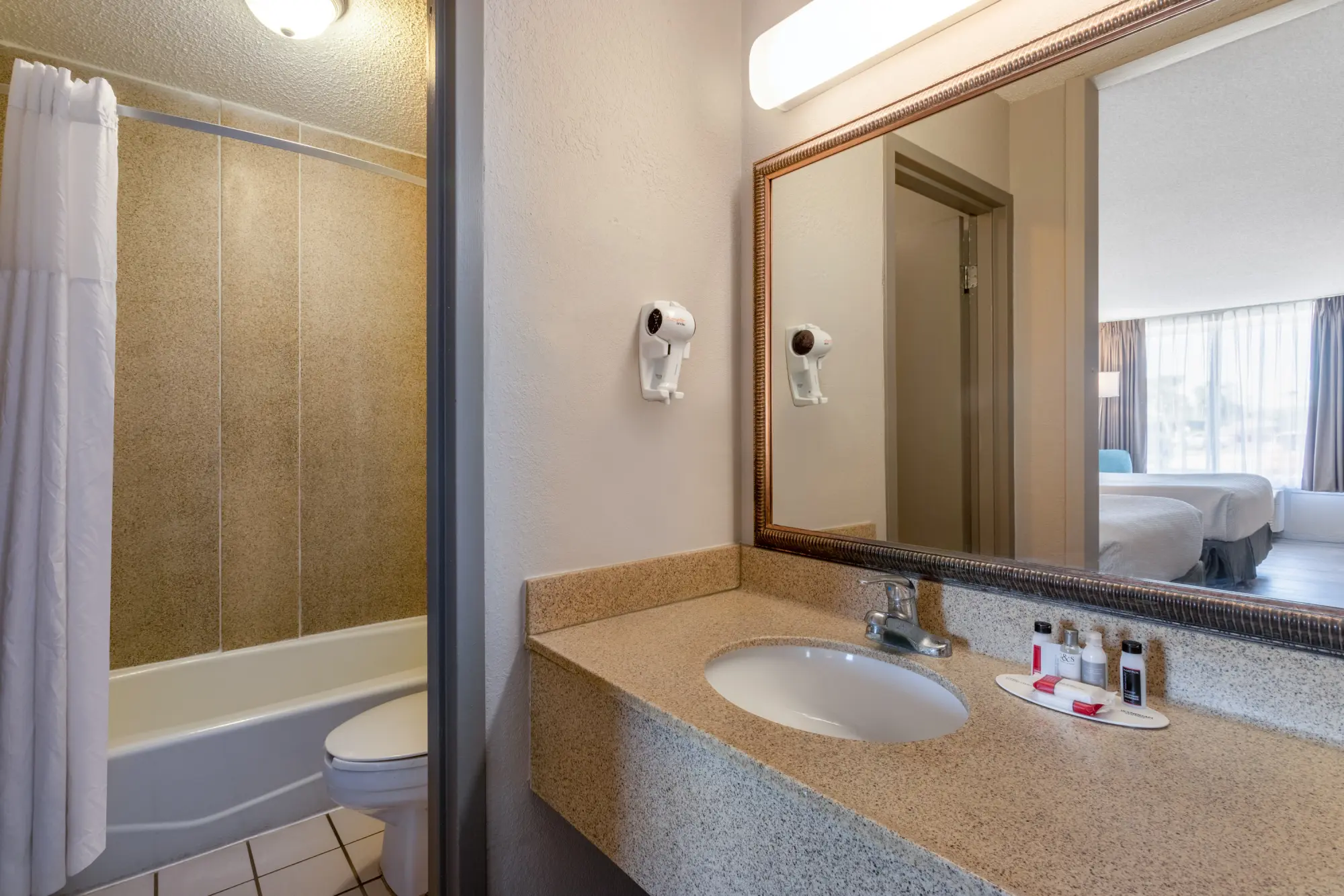 Days Inn Titusville hotel bathroom featuring a granite countertop with a sink, a wall-mounted hairdryer, and complimentary toiletries.