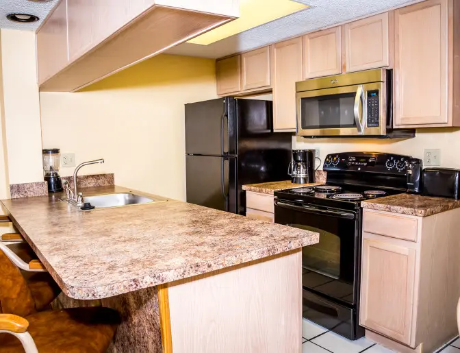 Fully equipped kitchen with a black refrigerator, stove, microwave, and brown wooden cabinets inside a guest room at the Ocean Landings Resort.