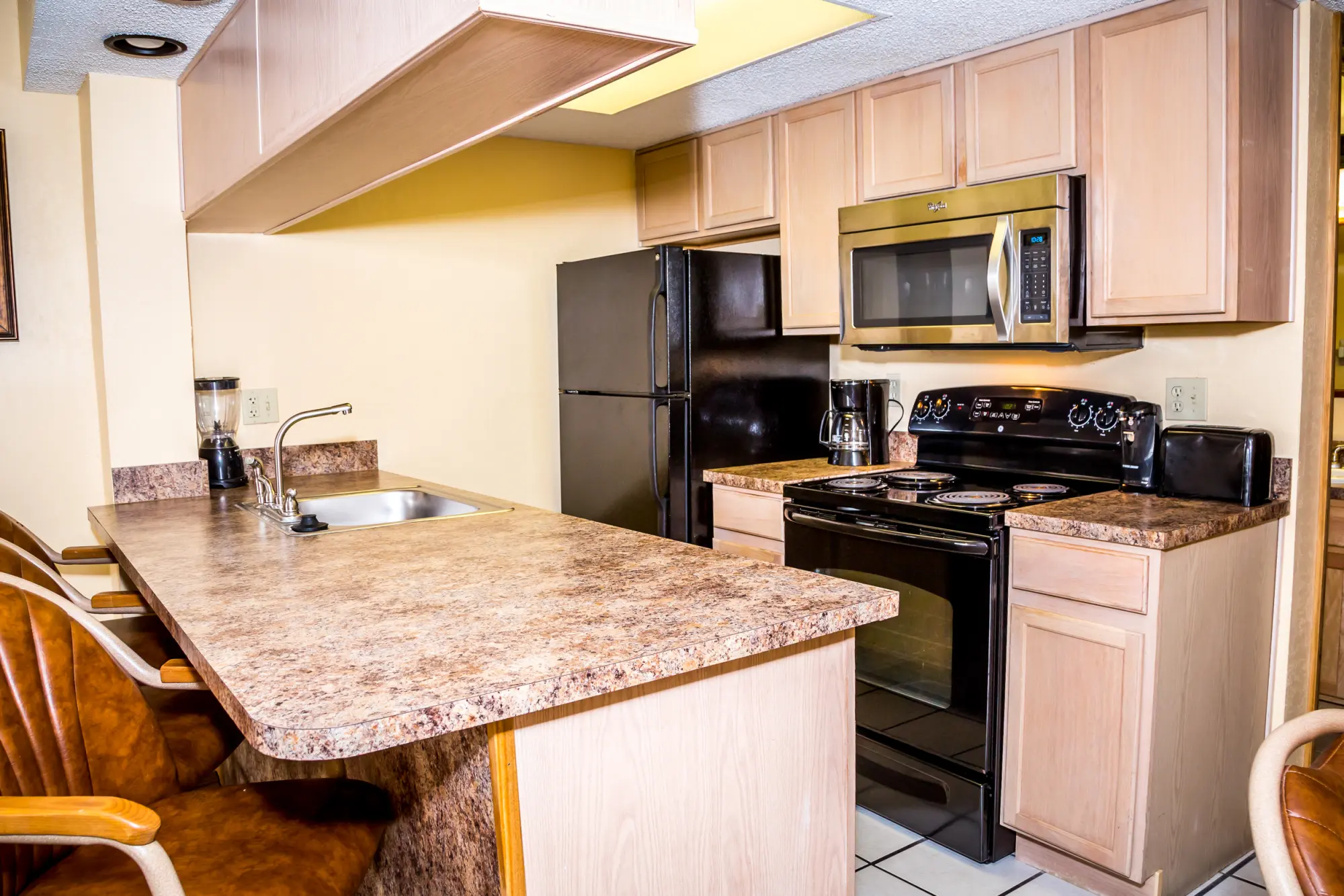 Fully equipped kitchen with a black refrigerator, stove, microwave, and brown wooden cabinets inside a guest room at the Ocean Landings Resort.