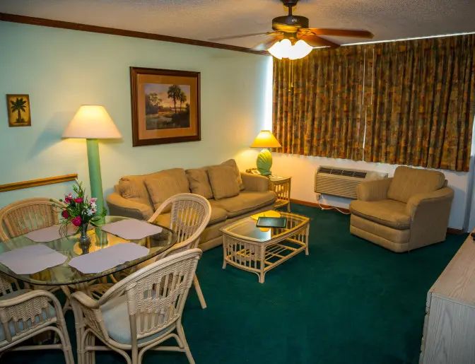 A cozy living room in Ocean Landings Resort with a sofa, armchairs, a dining table, and tropical-themed decor.