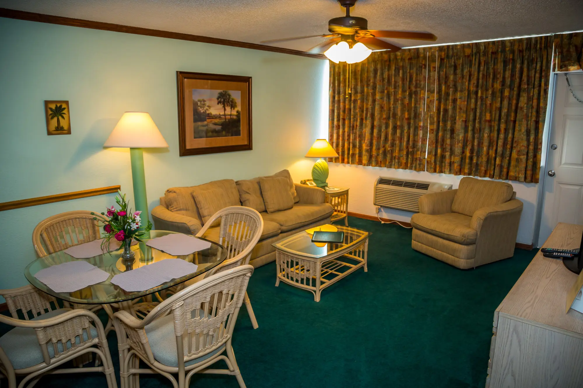 A cozy living room in Ocean Landings Resort with a sofa, armchairs, a dining table, and tropical-themed decor.