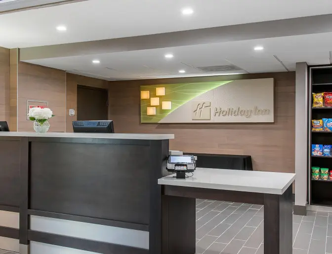 Holiday Inn hotel lobby with a modern front desk, flower arrangement, and a snack display shelf filled with assorted treats.