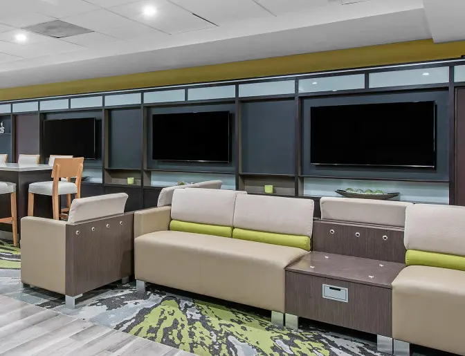 Modern hotel lobby at Holiday Inn with a mix of soft seating and high top tables, accented by large flat screen televisions.