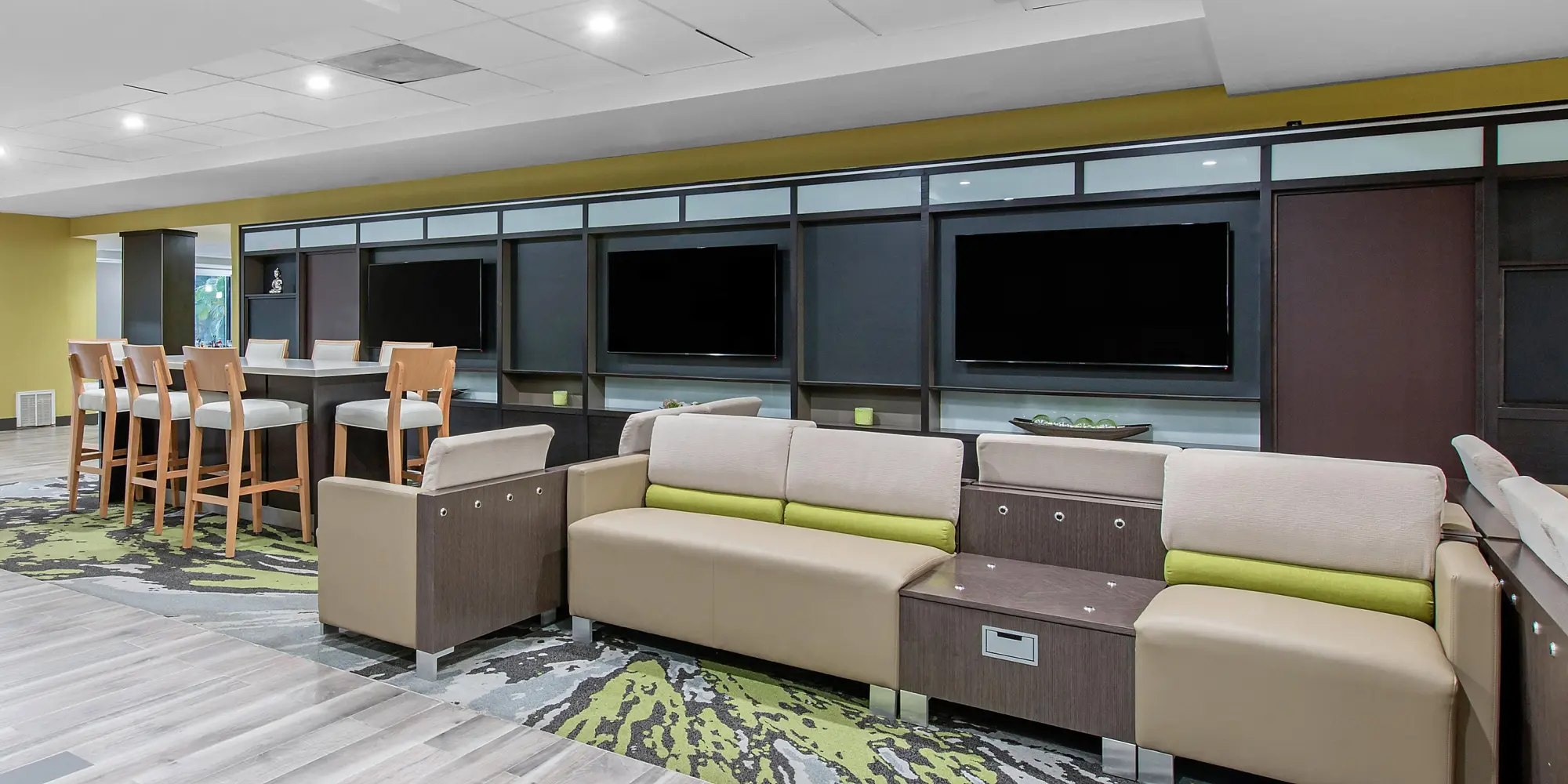 Modern hotel lobby at Holiday Inn with a mix of soft seating and high top tables, accented by large flat screen televisions.