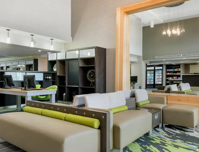 Holiday Inn lobby area with modern seating, computer workstations, and a mirror reflecting the snack bar and reception desk.