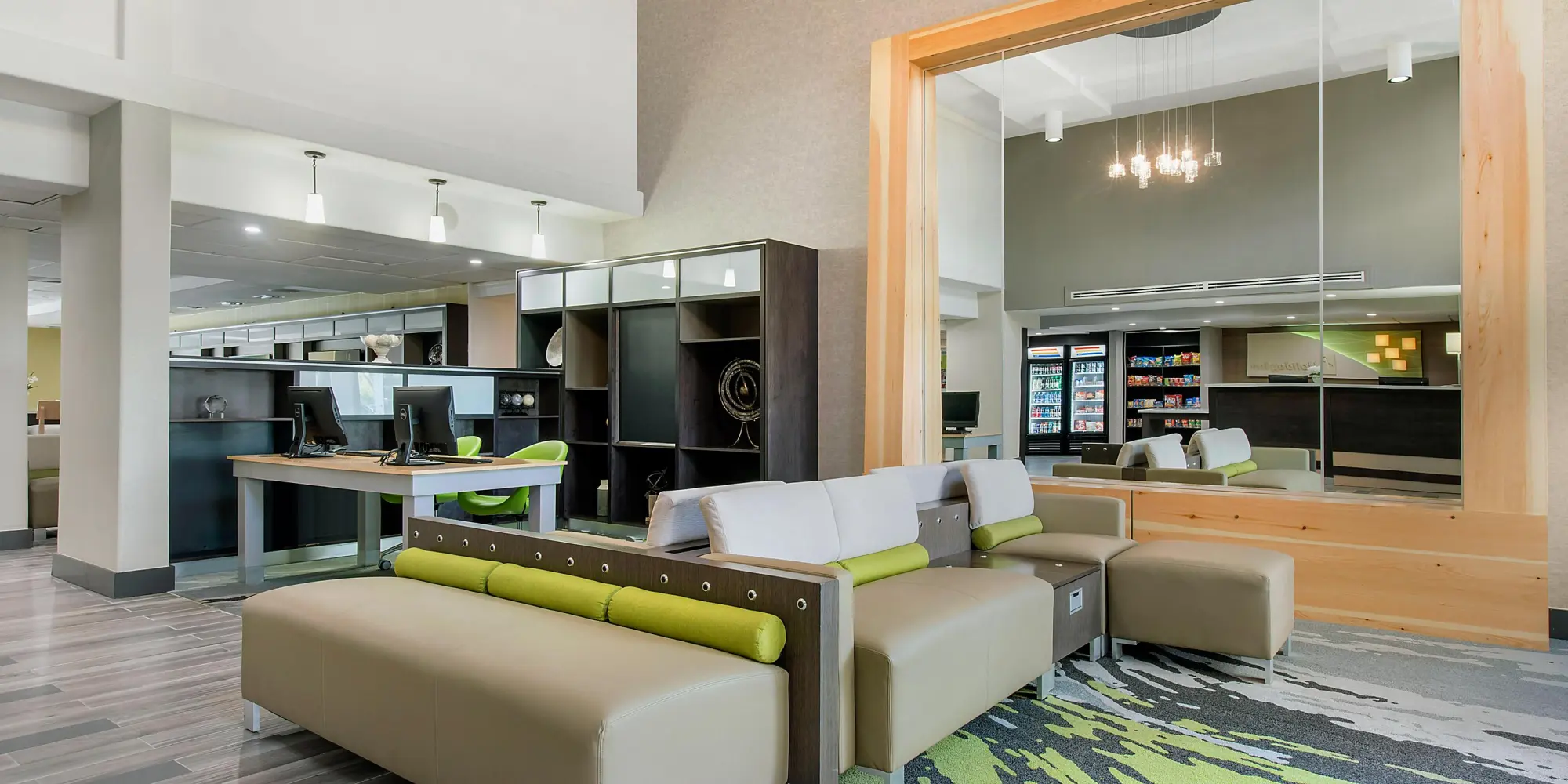 Holiday Inn lobby area with modern seating, computer workstations, and a mirror reflecting the snack bar and reception desk.