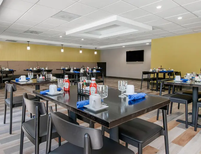 Hotel dining room at Holiday Inn featuring modern decor, tables set with glassware, and a warm yellow accent wall.