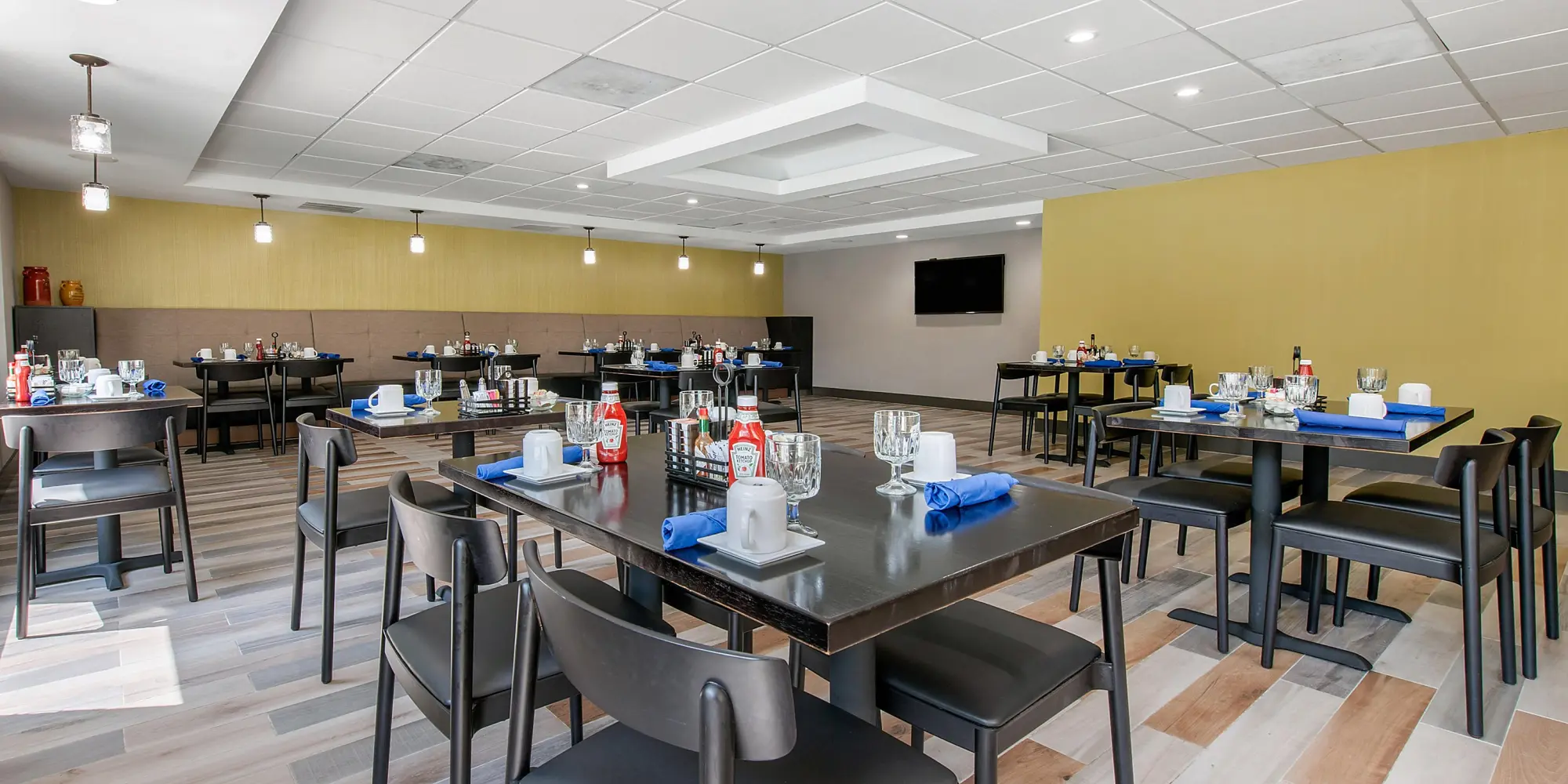 Hotel dining room at Holiday Inn featuring modern decor, tables set with glassware, and a warm yellow accent wall.