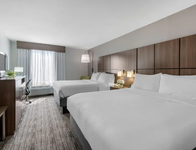 Contemporary guest room at Holiday Inn with two queen beds, stylish decor, and a large window with natural light.