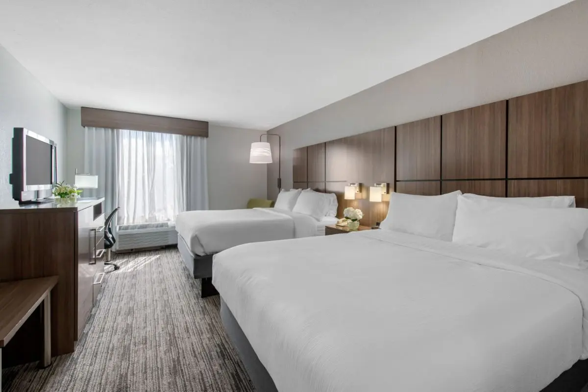 Contemporary guest room at Holiday Inn with two queen beds, stylish decor, and a large window with natural light.