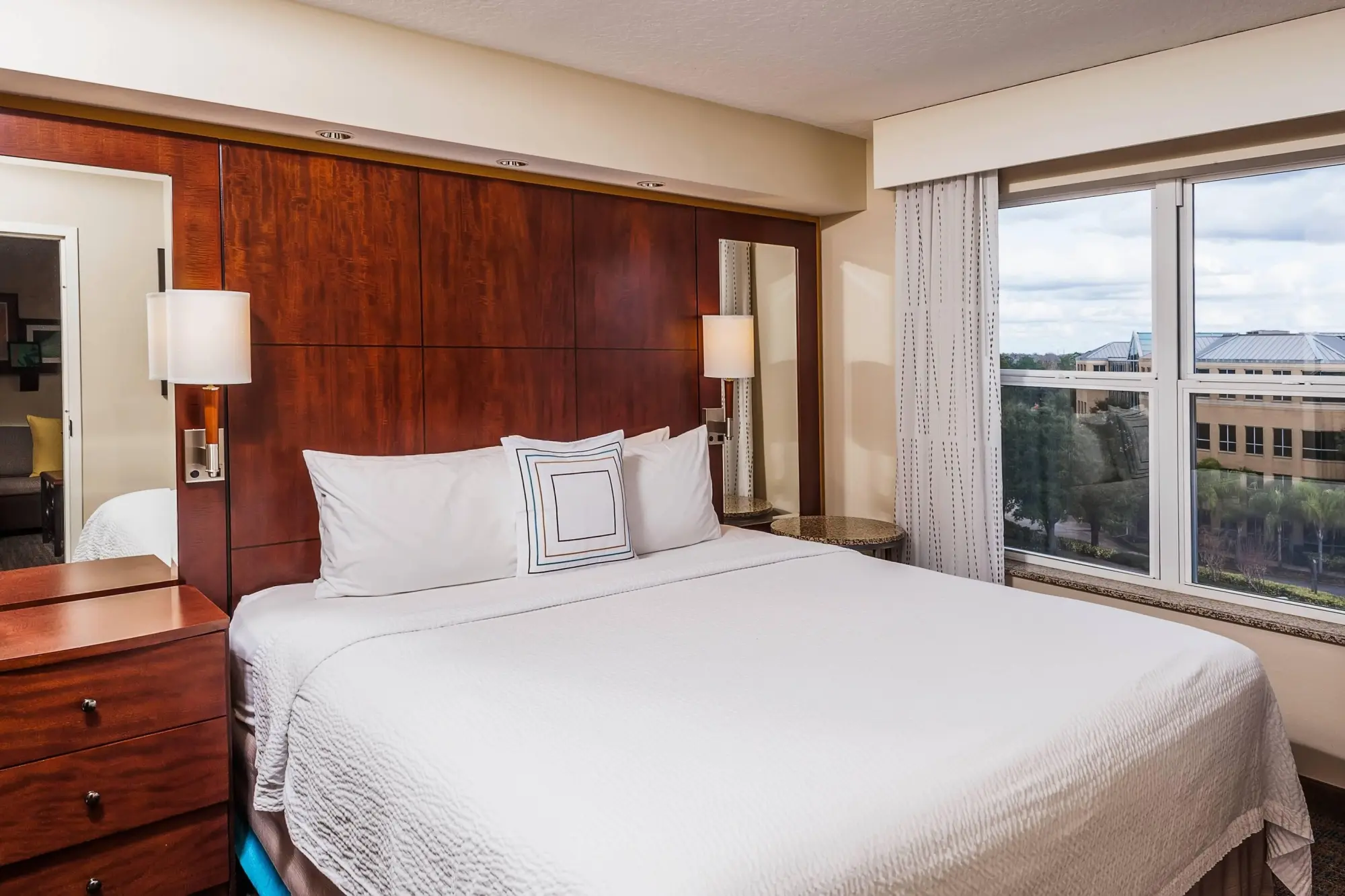 Hotel room with a king bed at Holiday Inn, featuring a sleek wooden headboard, bedside lighting, and a window with curtains.