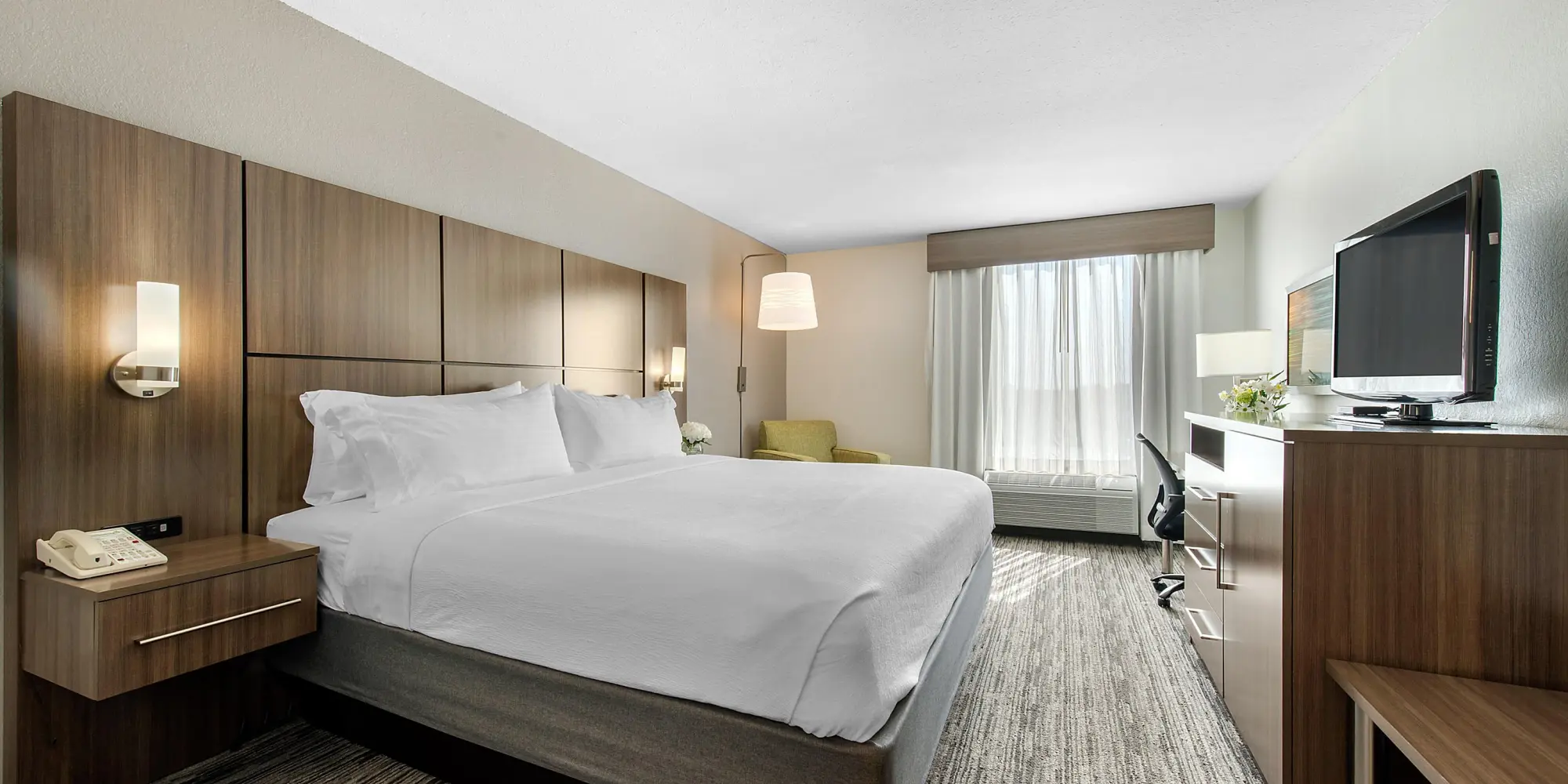 Hotel room at Holiday Inn with a king bed, sleek wooden furniture, and a flat-screen TV opposite the bed.