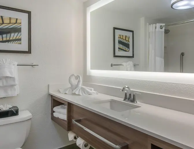 Modern hotel bathroom at Holiday Inn featuring a large backlit mirror, towel rack, and contemporary decor.