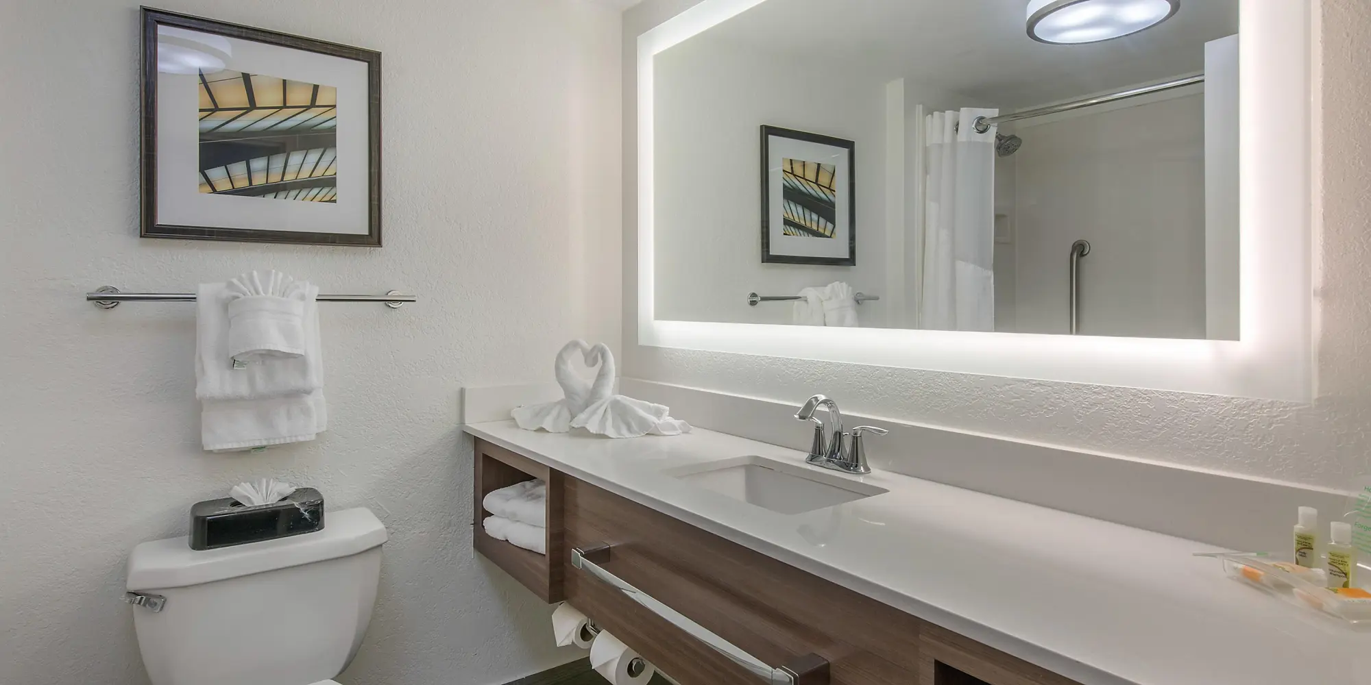 Modern hotel bathroom at Holiday Inn featuring a large backlit mirror, towel rack, and contemporary decor.