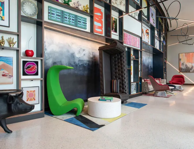 Artistic hotel lobby with eclectic decor, including modern art displays, colorful chairs, and creative sculptures against a geometric wall.