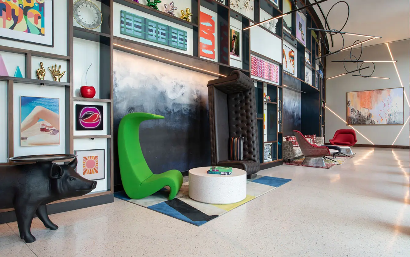 Artistic hotel lobby with eclectic decor, including modern art displays, colorful chairs, and creative sculptures against a geometric wall.