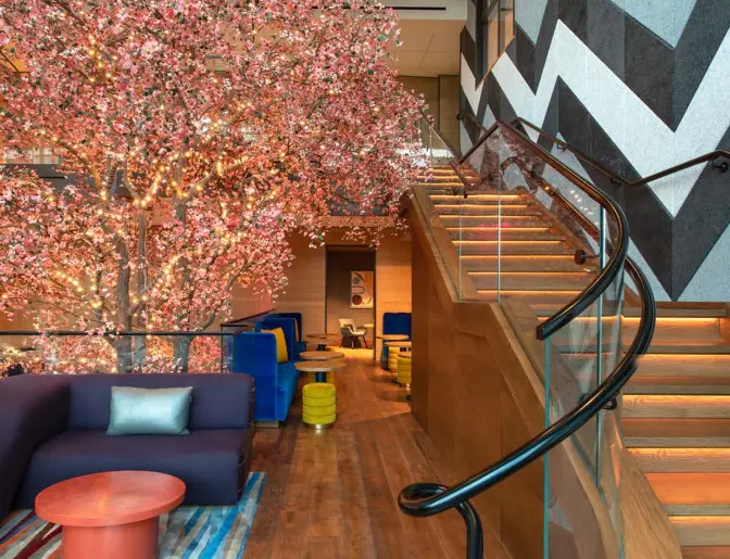 Lobby area at the Lake Nona Wave Hotel featuring a large illuminated cherry blossom tree next to a winding staircase with modern wood and glass accents.
