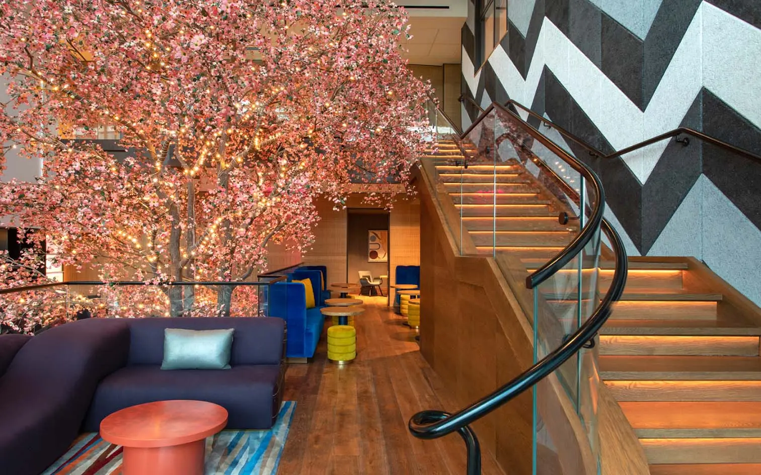 Lobby area at the Lake Nona Wave Hotel featuring a large illuminated cherry blossom tree next to a winding staircase with modern wood and glass accents.