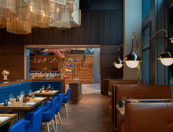 Modern dining area with blue booth seating and tan chairs, illuminated by sleek pendant lights and accented with wooden design elements.