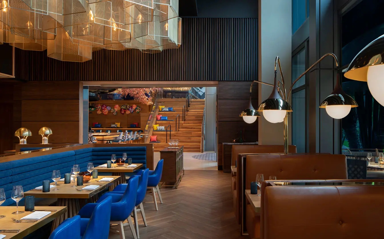 Modern dining area with blue booth seating and tan chairs, illuminated by sleek pendant lights and accented with wooden design elements.