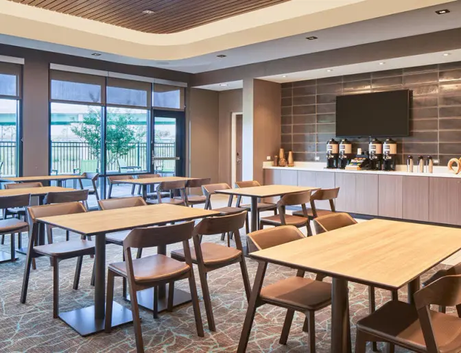 Modern dining space at SpringHill Suites Lake Nona, with sleek wooden furniture, a coffee station, and large windows allowing natural light to fill the room.