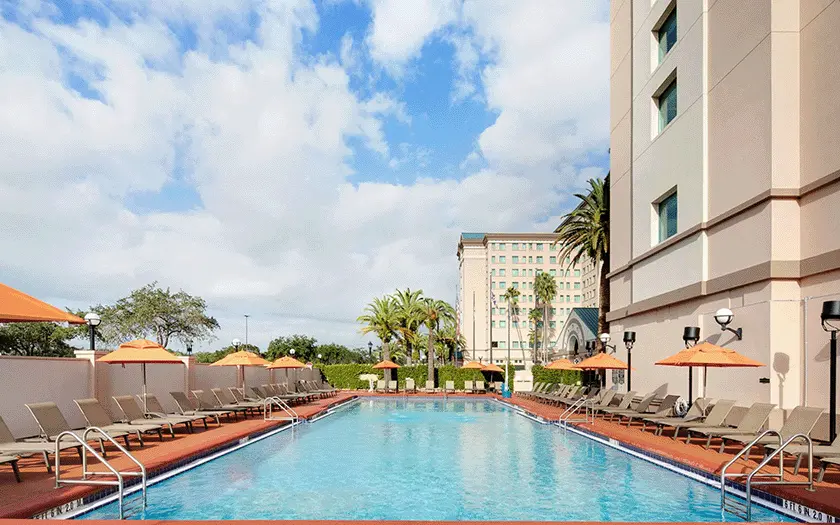 Outdoor pool at the Florida Hotel on a bright sunny day featuring orange umbrellas and tan lounge chairs.