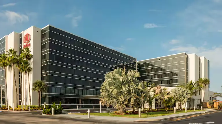 Street view of the Hilton Cocoa Beach Oceanfront hotel featuring modern glass architecture, tall palm trees, and a well-maintained tropical landscape.