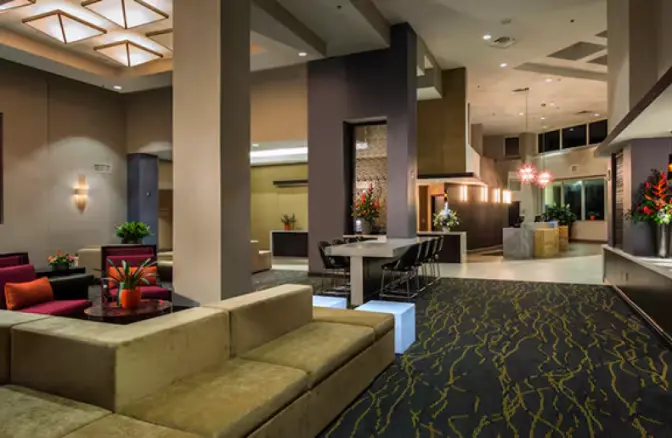 Spacious hotel lobby at Hilton Cocoa Beach featuring modern seating arrangements, vibrant floral displays, a patterned carpet, and illuminated ceiling fixtures.