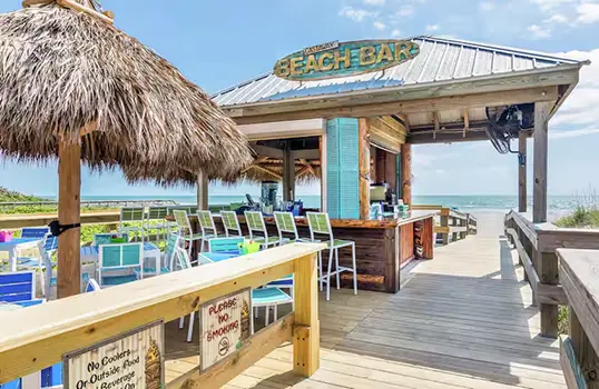 Thatched-roof beach bar at Hilton Cocoa Beach with oceanfront views, colorful chairs, and a wooden boardwalk leading to the sand.