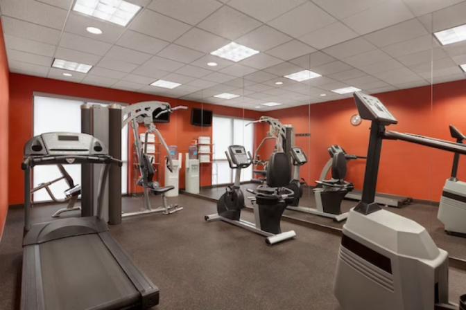 Ramada Suites fitness center featuring a variety of modern exercise equipment, including treadmills, stationary bikes, free weights, and large mirrors on the walls for an open and spacious feel.