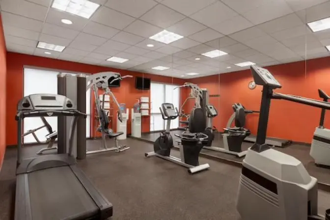 Ramada Suites fitness center featuring a variety of modern exercise equipment, including treadmills, stationary bikes, free weights, and large mirrors on the walls for an open and spacious feel.