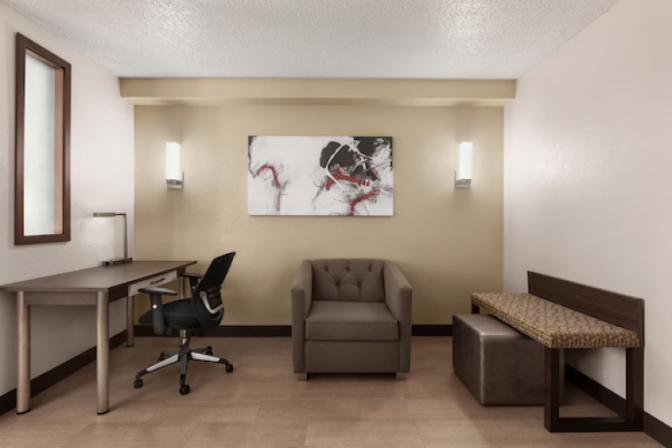 Ramada Suites queen room with a cozy queen nook featuring a comfortable chair, a desk and a bench.