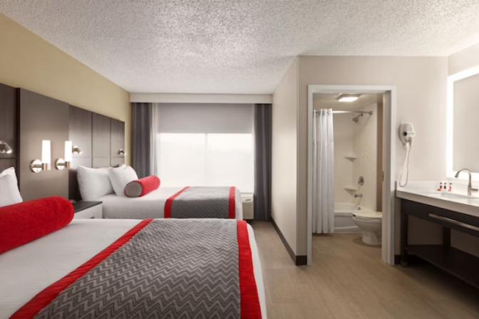 Modern queen room at Ramada Suites featuring  two comfortable queen sized beds with crisp white linens, a stylish headboard, bedside tables with lamps, a work desk, and contemporary decor.