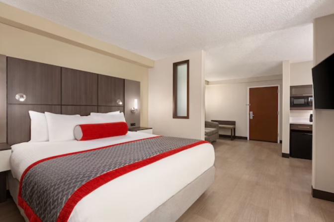 Modern king room at Ramada Suites featuring  a comfortable king sized bed a kitchenette and a sitting area.